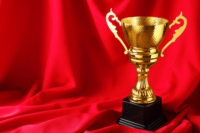 Golden trophy cup on red fabric. Space for text