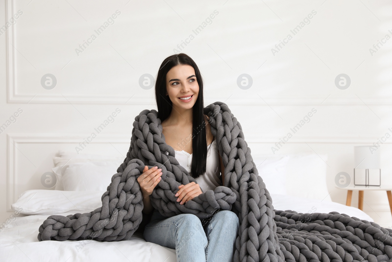 Photo of Young woman with chunky knit blanket on bed at home