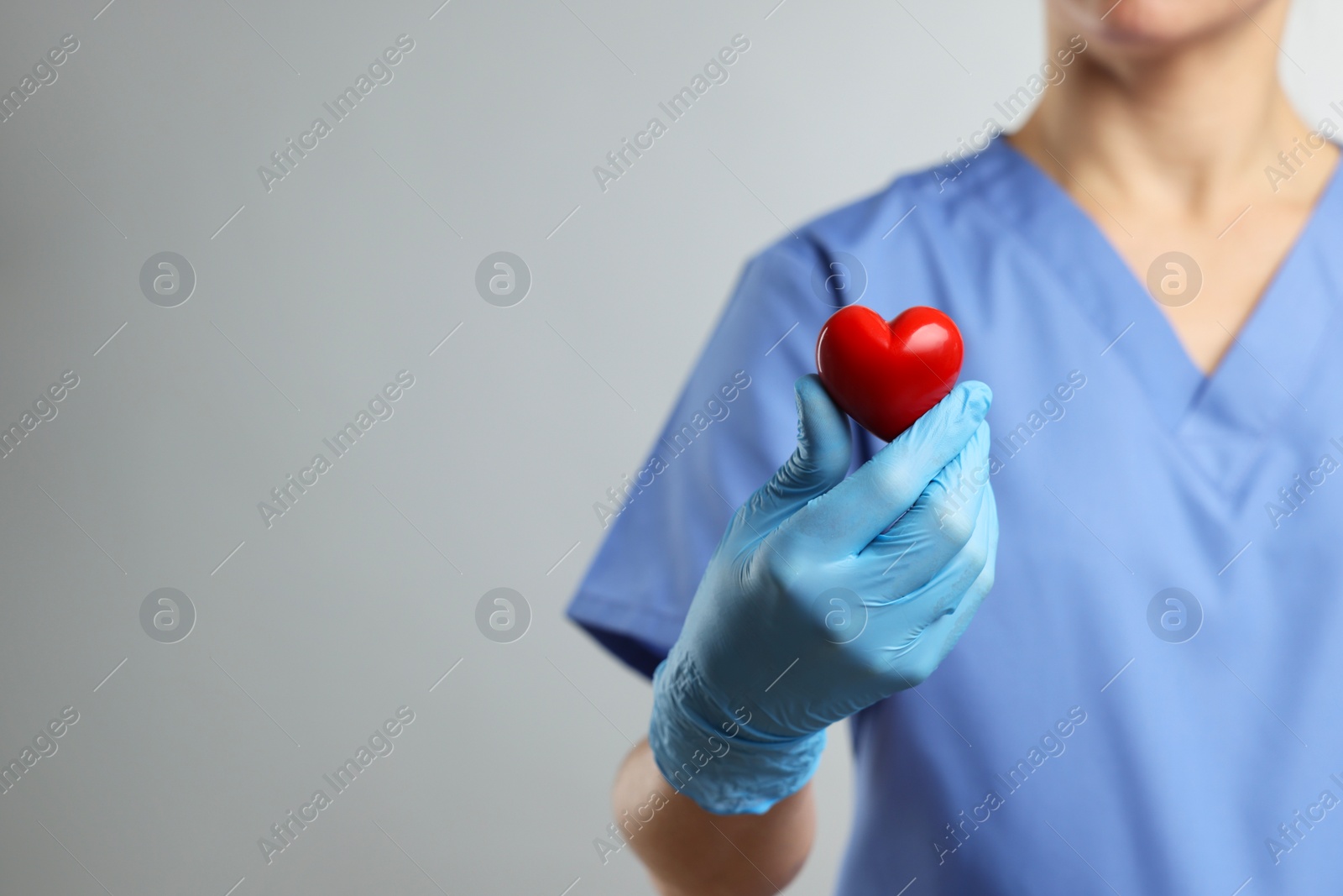 Photo of Doctor wearing light blue medical glove holding decorative heart on grey background, closeup. Space for text