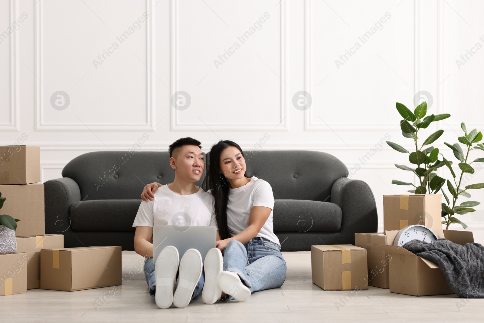 Photo of Happy couple with laptop on floor in their new apartment