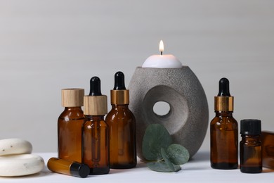 Different aromatherapy products, burning candle and eucalyptus leaves on white wooden table