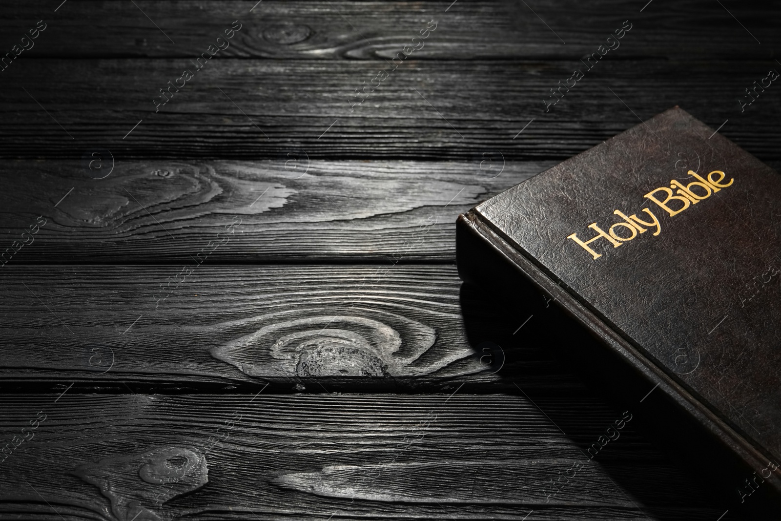 Photo of Bible with dark cover on black wooden table, space for text. Christian religious book