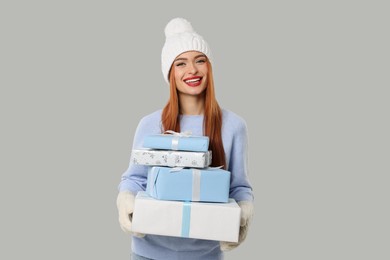 Photo of Young woman in hat and sweater with Christmas gifts on light grey background