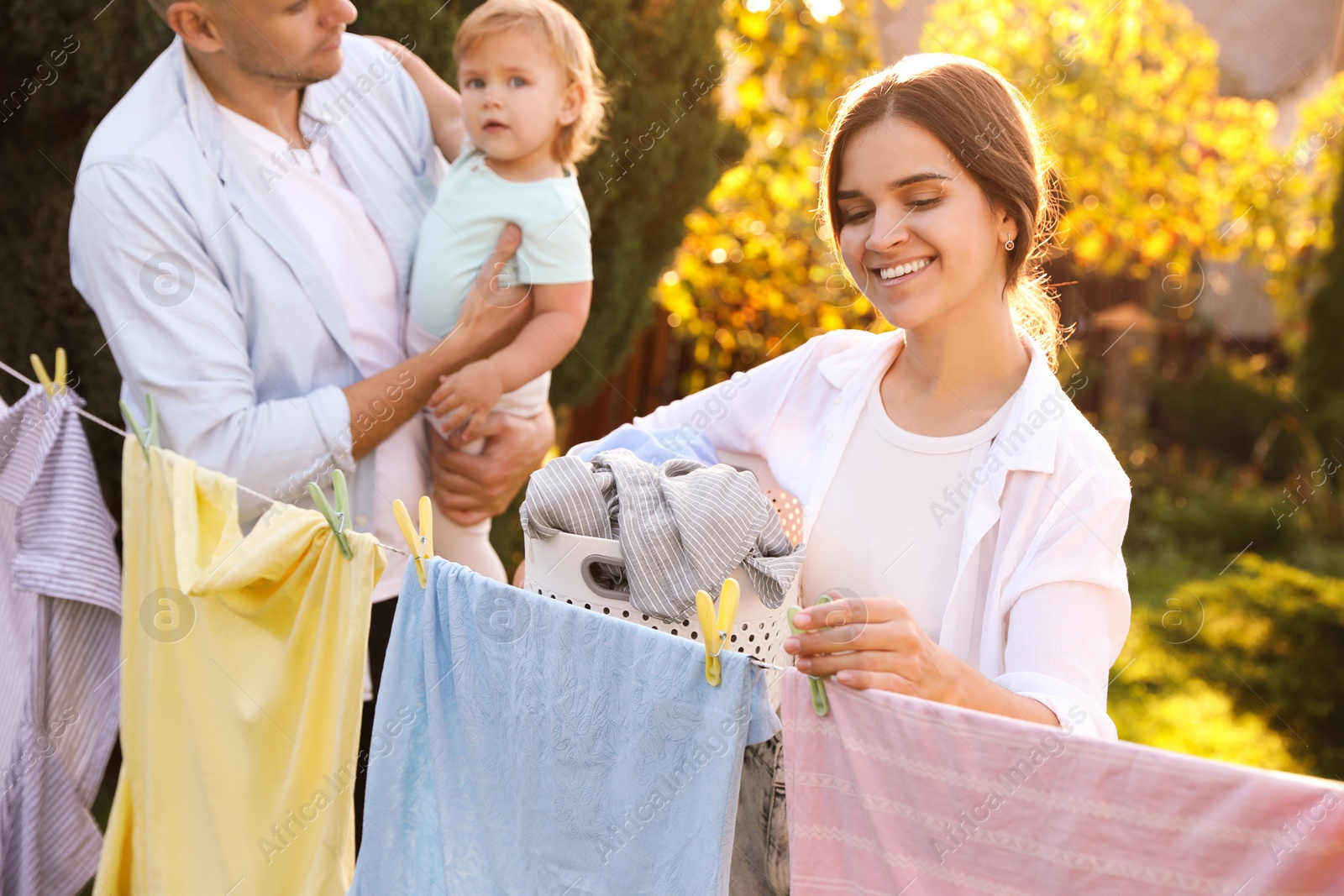 Photo of Woman hanging clothes with clothespins on washing line for drying in backyard