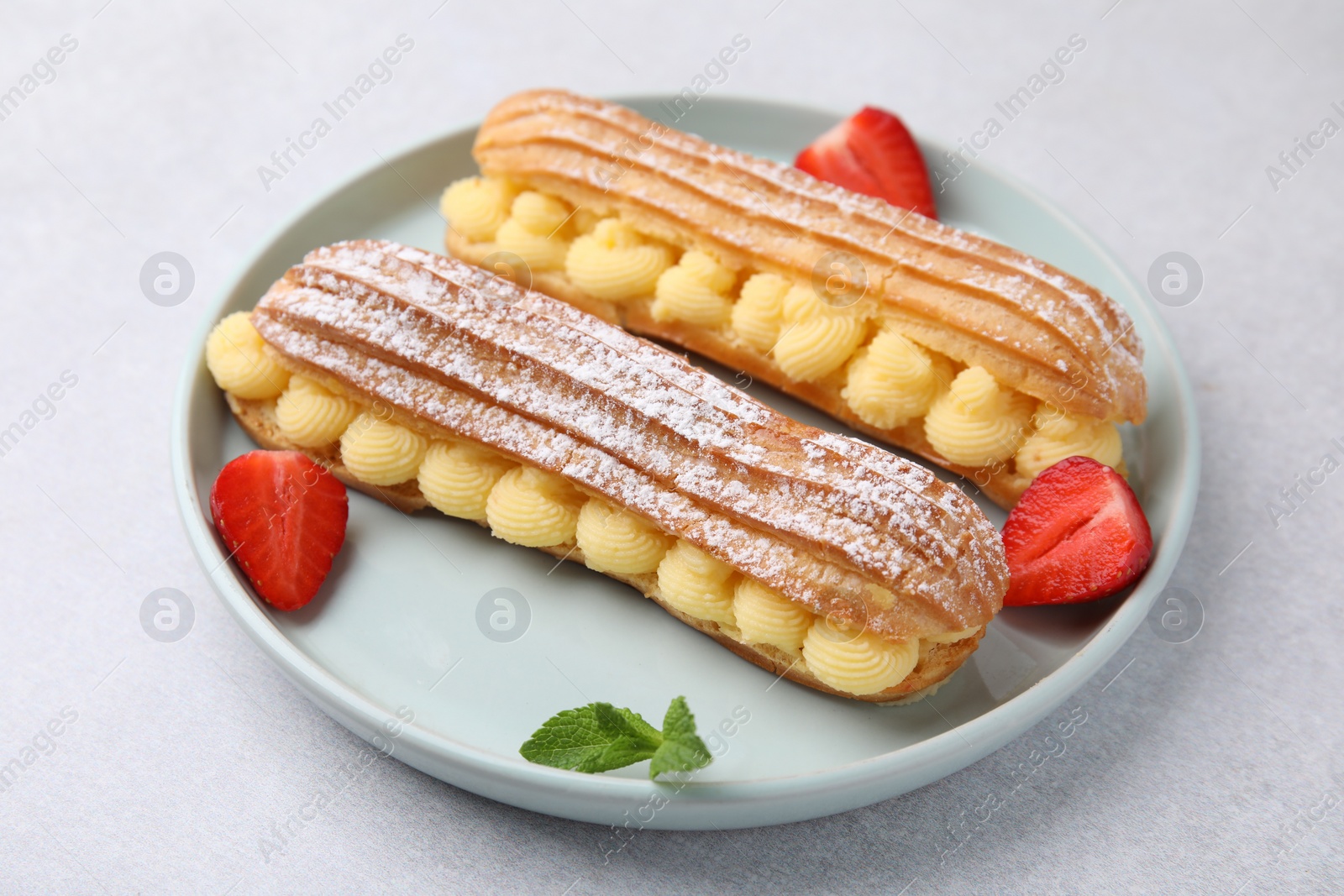 Photo of Delicious eclairs filled with cream, strawberries and mint on light table