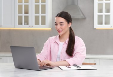 Photo of Woman using laptop at white table in kitchen