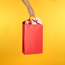 Photo of Woman holding paper shopping bag full of gift boxes on yellow background, closeup