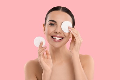 Beautiful woman removing makeup with cotton pads on pink background