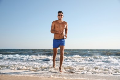 Photo of Handsome man with attractive body running on beach