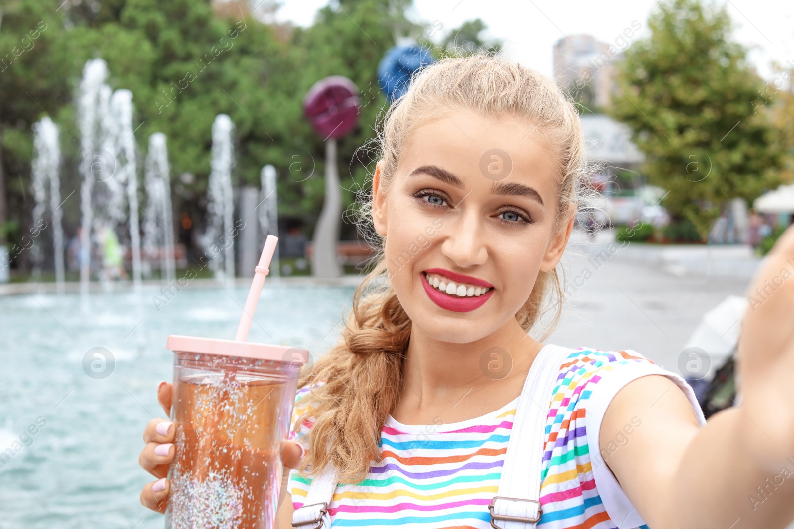 Photo of Attractive woman taking selfie near fountain in park