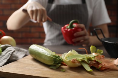 Photo of Woman with bell pepper, peels of fresh vegetables on table indoors, selective focus