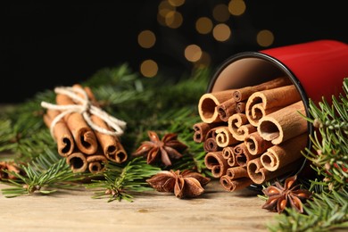 Photo of Many cinnamon sticks, anise stars and fir branches on wooden table, closeup. Space for text