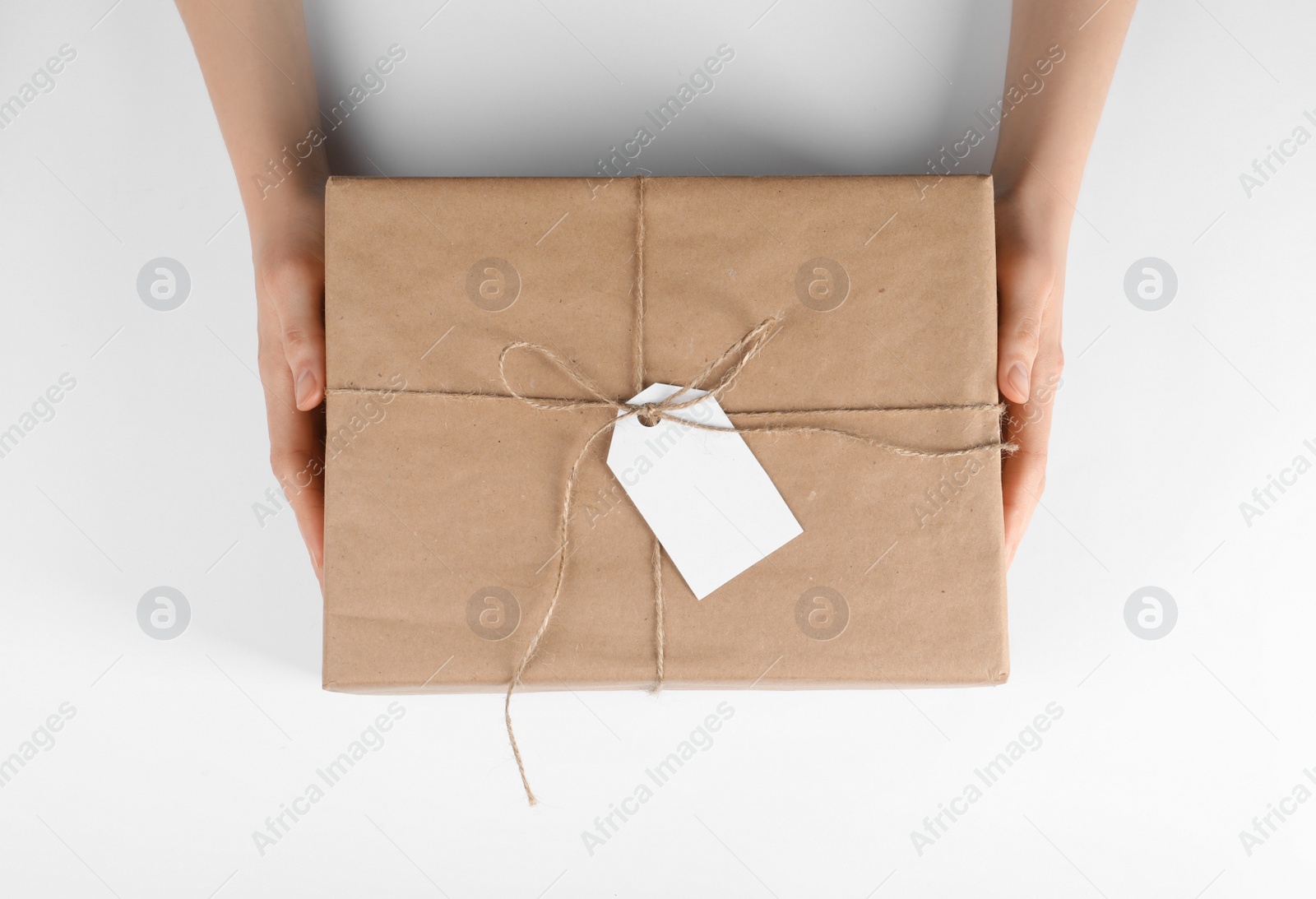 Photo of Woman holding parcel wrapped in kraft paper with tag on white background, top view