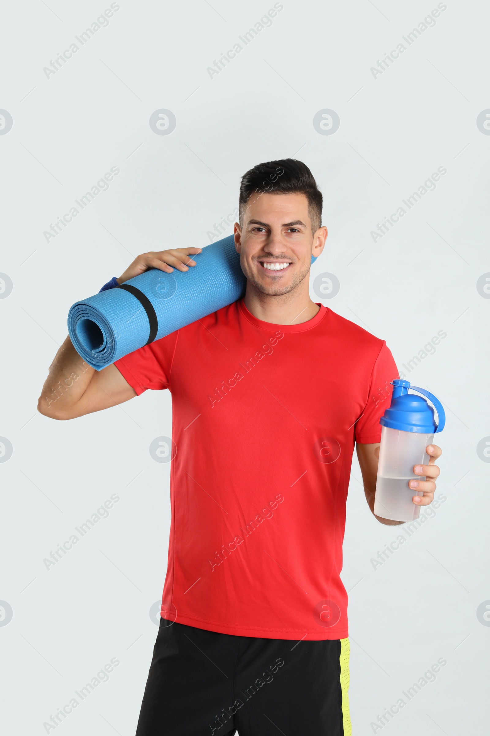 Photo of Handsome man with yoga mat and shaker on light background