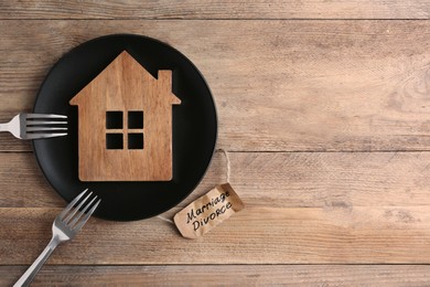 Divorce concept. Plate with model of house and forks near paper card on wooden table, flat lay. Space for text