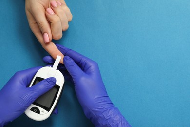 Diabetes. Doctor checking patient's blood sugar level with glucometer on blue background, top view. Space for text