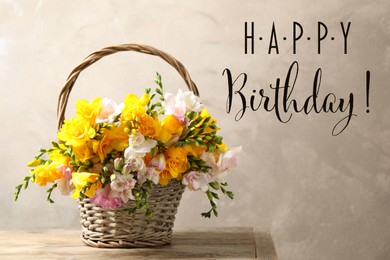 Happy Birthday! Beautiful freesia flowers in wicker basket on table 