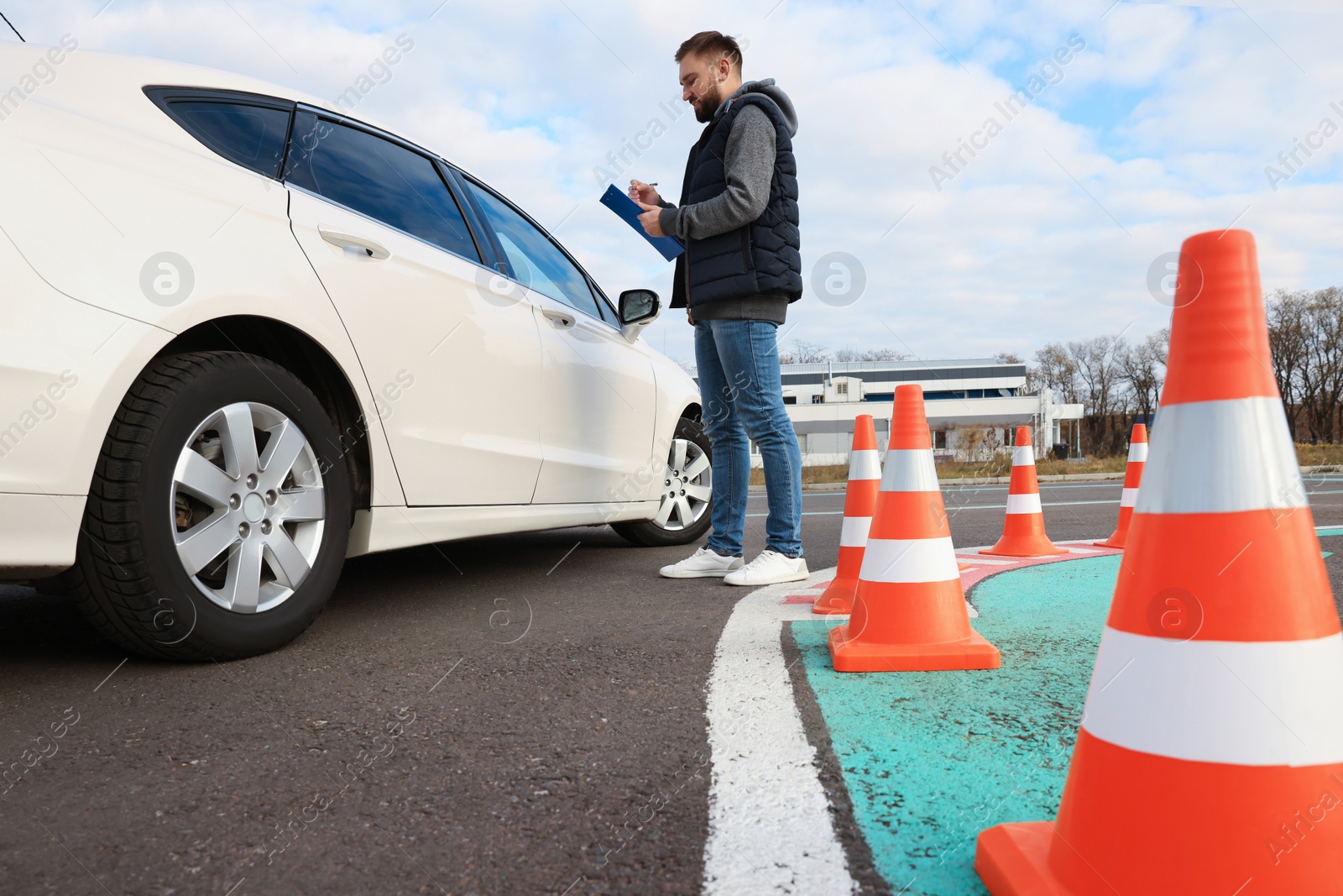 Photo of Instructor with clipboard near car outdoors, low angle view. Driving school exam