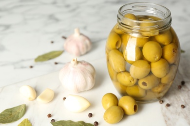 Photo of Glass jar of pickled olives on white table, closeup. Space for text
