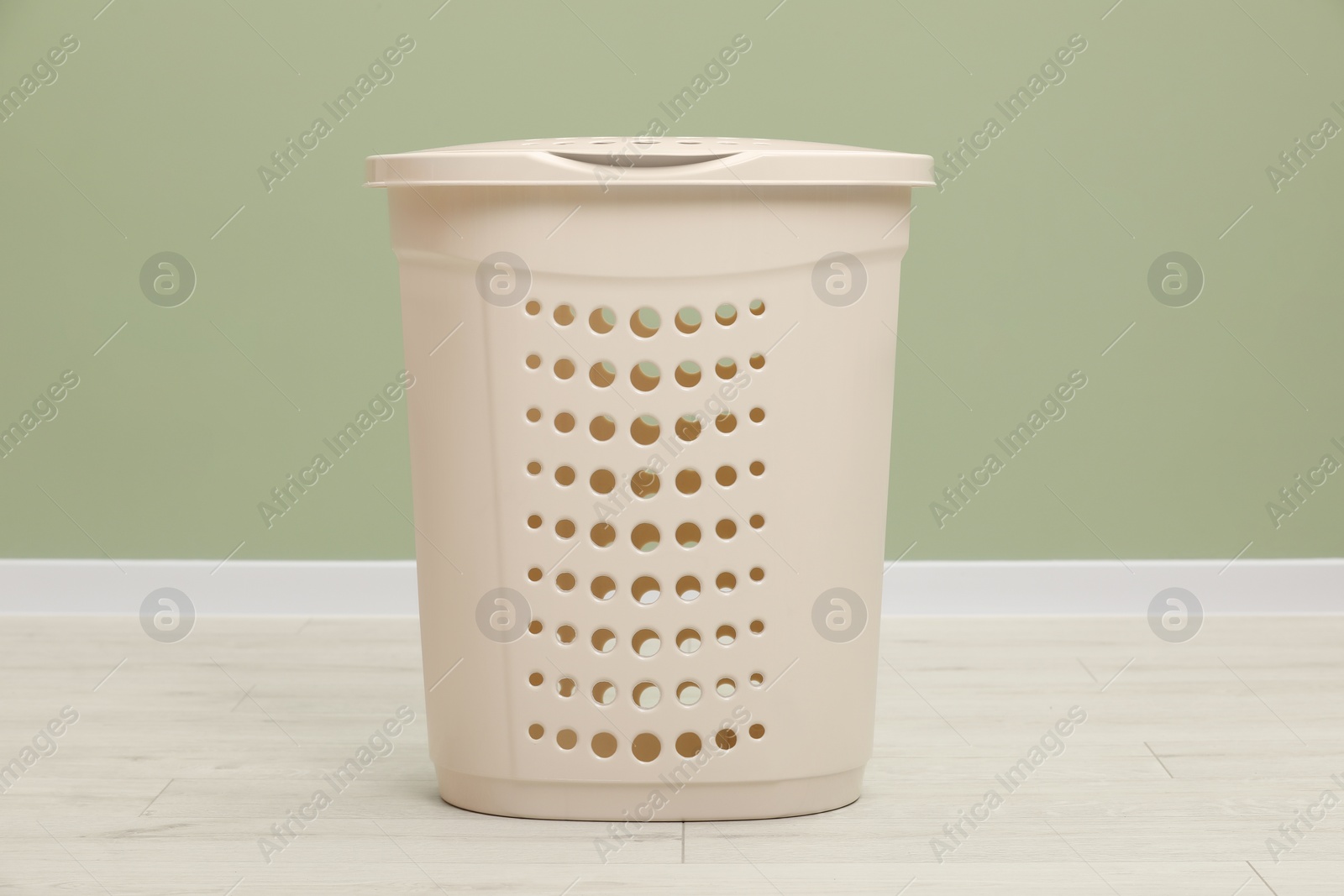 Photo of Empty plastic laundry basket near light green wall