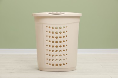 Empty plastic laundry basket near light green wall