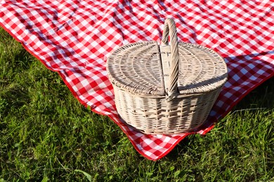 Picnic basket with checkered tablecloth on green grass outdoors