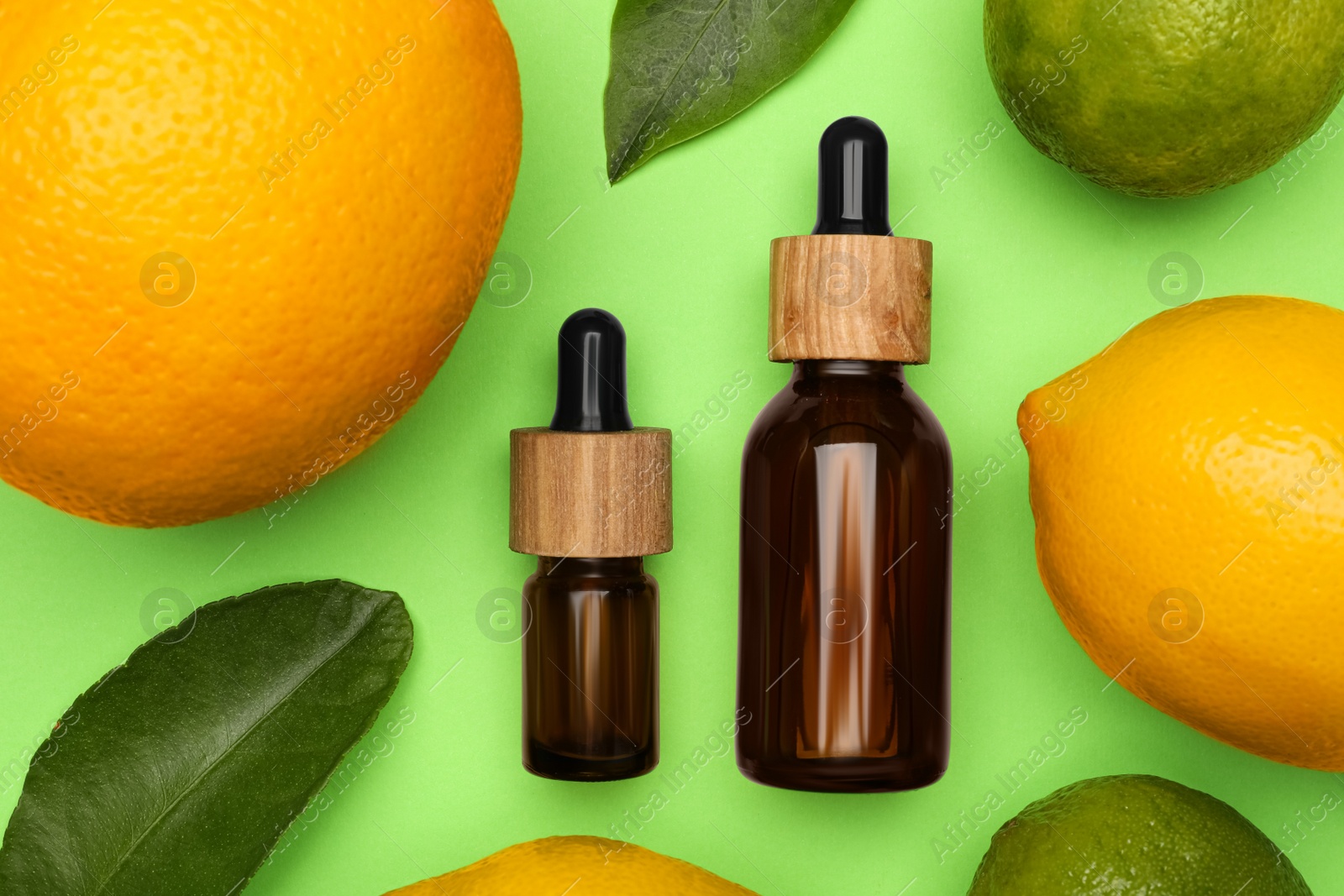 Photo of Bottles of citrus essential oil and fresh fruits on green background, flat lay