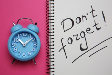 Photo of Alarm clock and notebook with text Don't forget on pink background, flat lay. Reminder concept