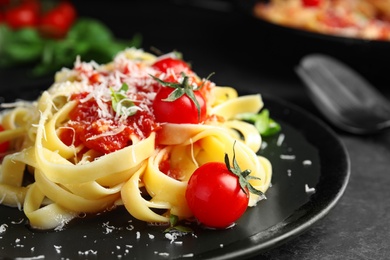 Photo of Tasty pasta with basil, tomatoes and cheese on black table, closeup