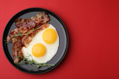 Photo of Fried eggs, bacon and microgreens on red background, top view. Space for text