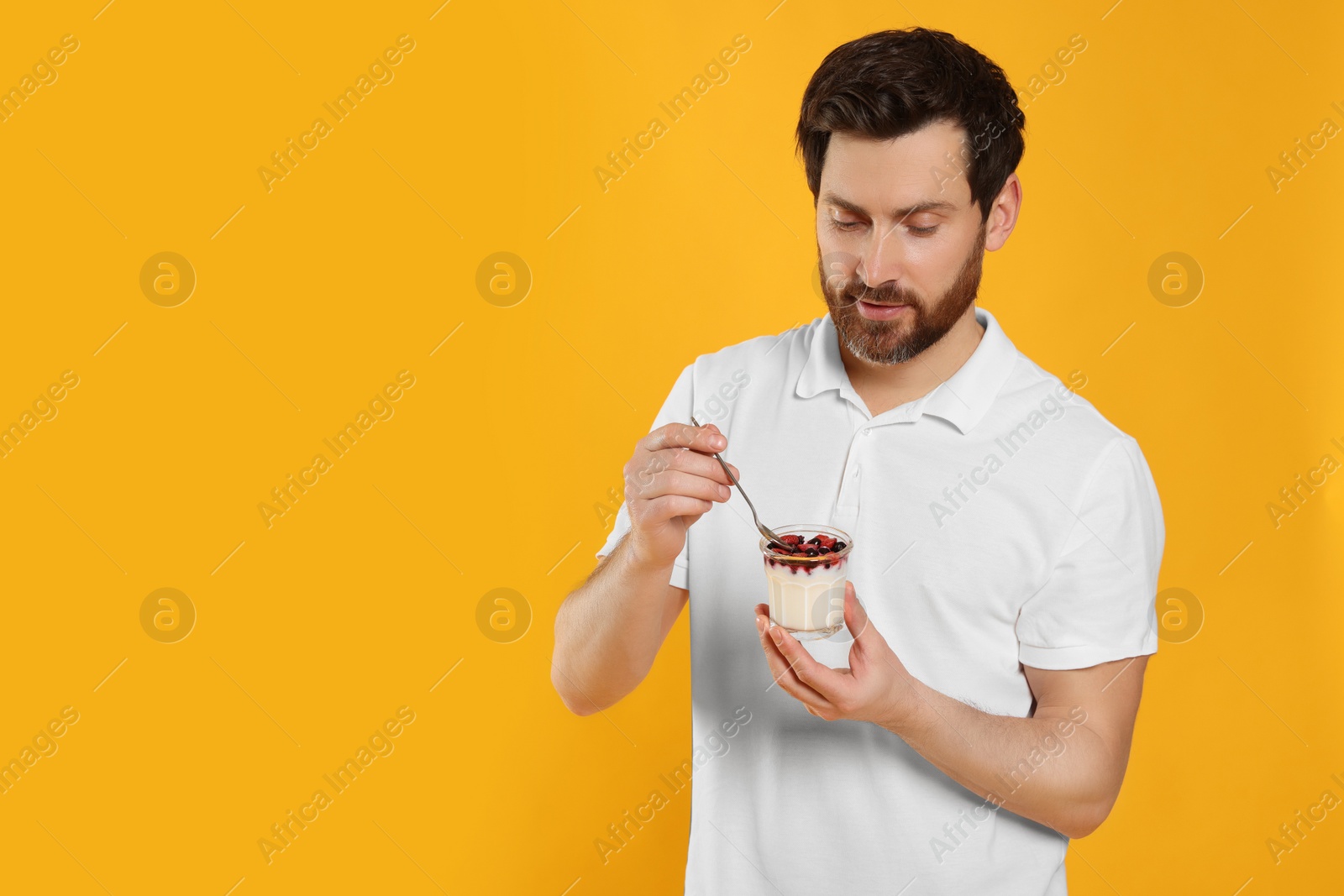 Photo of Handsome man with delicious yogurt and spoon on yellow background. Space for text