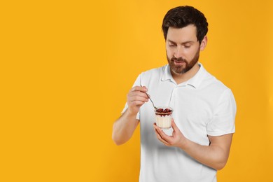 Photo of Handsome man with delicious yogurt and spoon on yellow background. Space for text