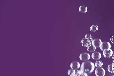 Photo of Beautiful transparent soap bubbles on purple background, space for text