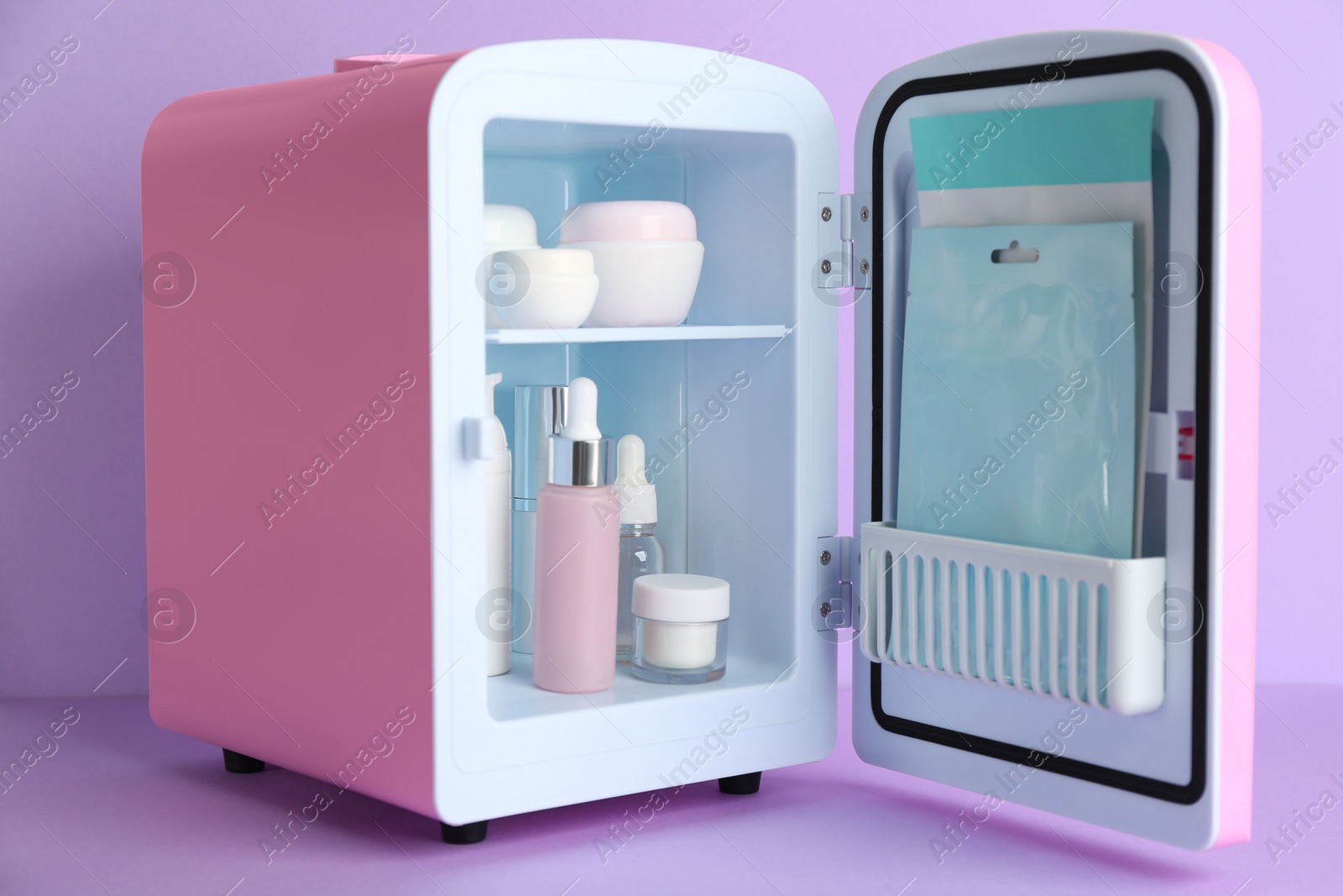 Photo of Open cosmetic refrigerator with skin care products on violet background