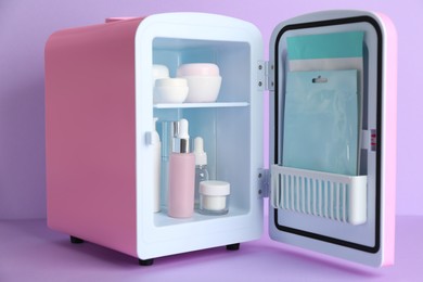 Open cosmetic refrigerator with skin care products on violet background