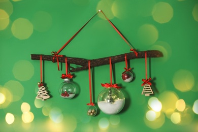 Image of Beautiful Christmas decoration of tree branch and holiday ornaments hanging on green wall, bokeh effect