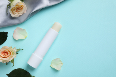 Photo of Hygienic lipstick and rose flowers on turquoise background, flat lay. Space for text