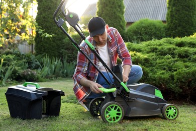 Photo of Man cleaning lawn mower with brush in garden