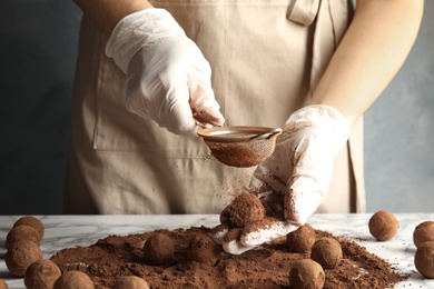 Woman preparing tasty chocolate truffles at table, closeup