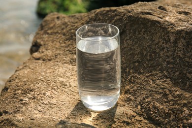 Photo of Glass of fresh water on stone outdoors