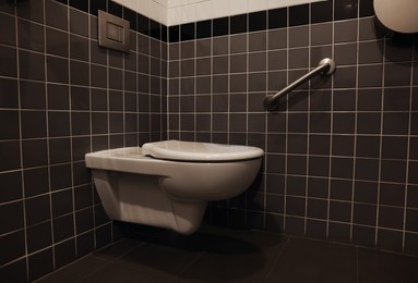 Photo of Clean ceramic toilet bowl near tiled wall indoors