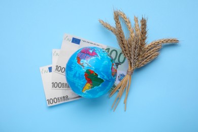 Photo of Import and export concept. Globe, ears of wheat and banknotes on light blue background, flat lay