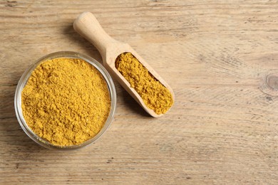 Photo of Curry powder in bowl and scoop on wooden table, top view. Space for text