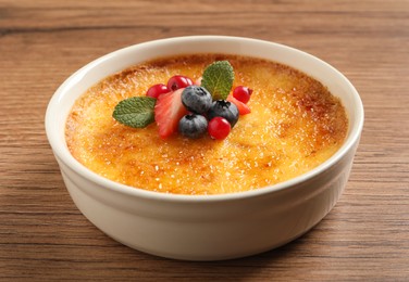 Photo of Delicious creme brulee with fresh berries on wooden table, closeup view