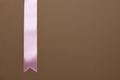 Beautiful pink ribbon on brown background, top view. Space for text