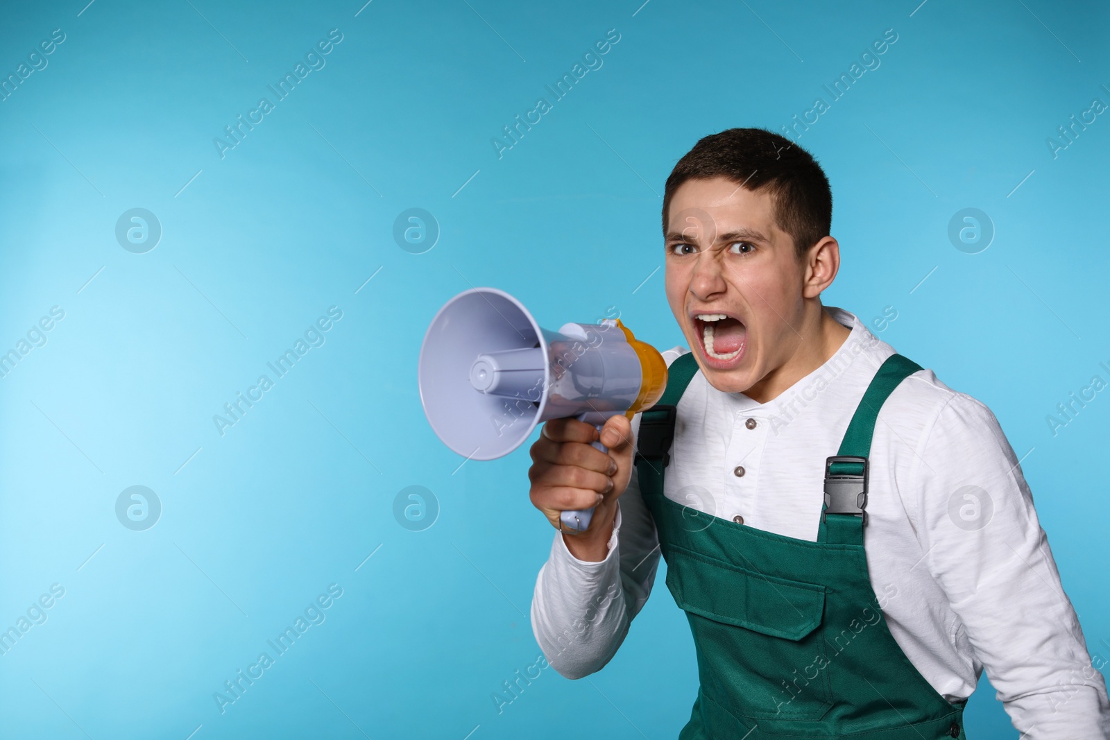 Photo of Portrait of emotional male worker using megaphone on color background. Space for text