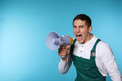 Portrait of emotional male worker using megaphone on color background. Space for text