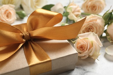 Photo of Golden gift box and beautiful roses on white marble table, closeup