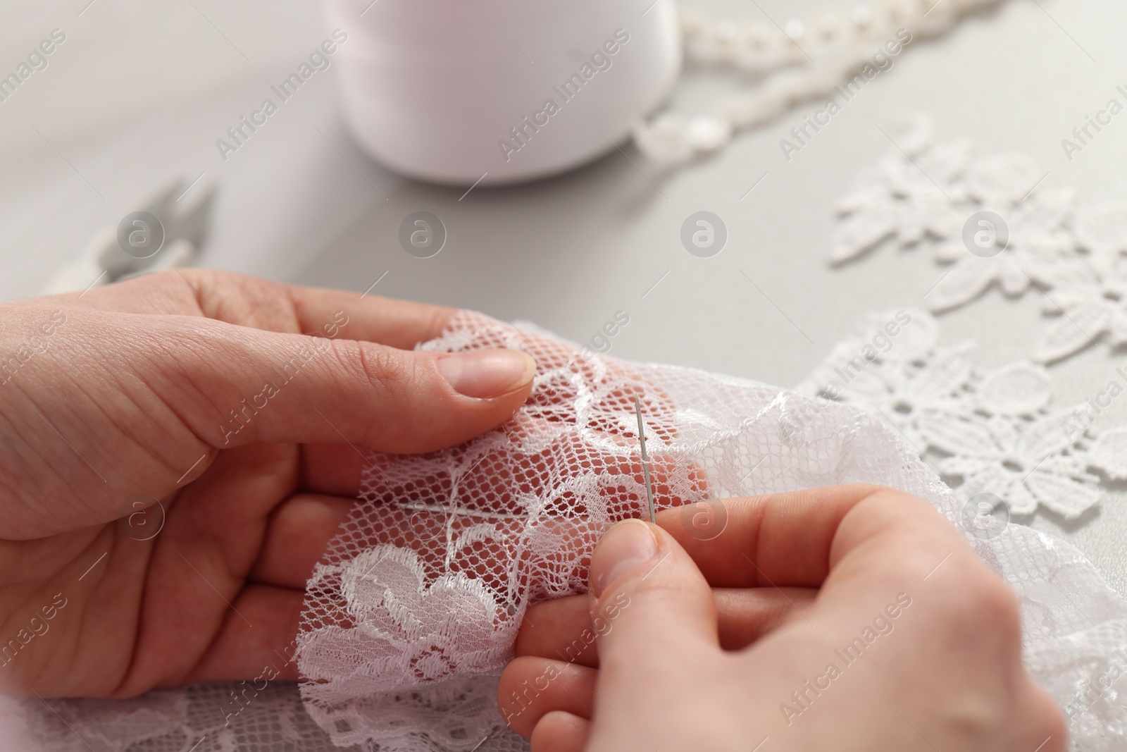 Photo of Dressmaker working with beautiful white lace at table in atelier, closeup