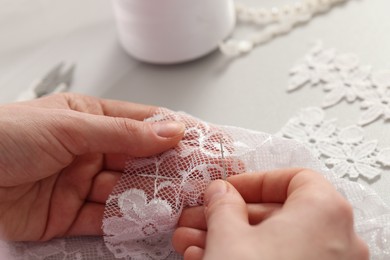 Dressmaker working with beautiful white lace at table in atelier, closeup